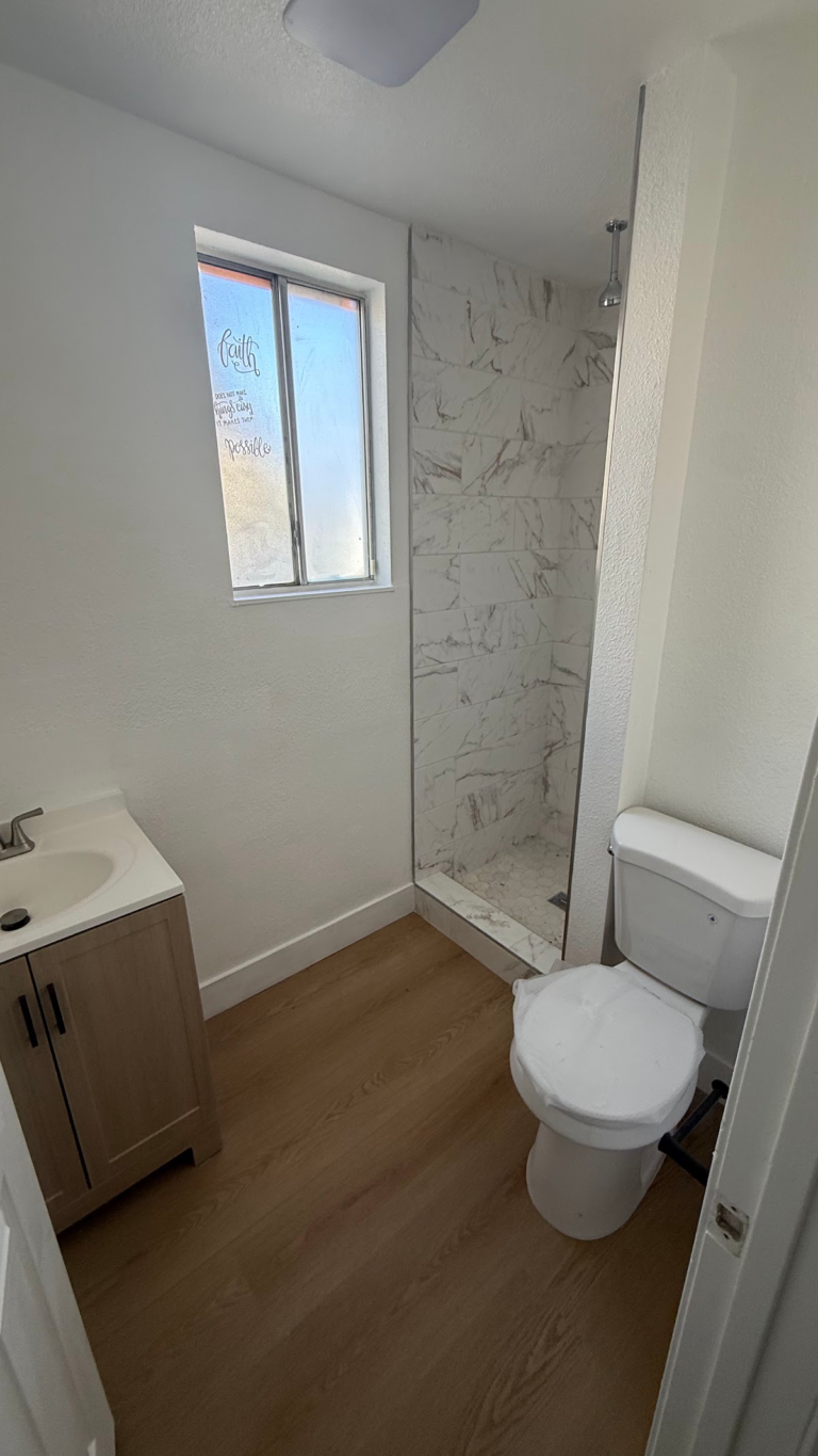 Bathroom shower and toilet with wood-look floor during the Las Vegas home restoration project.