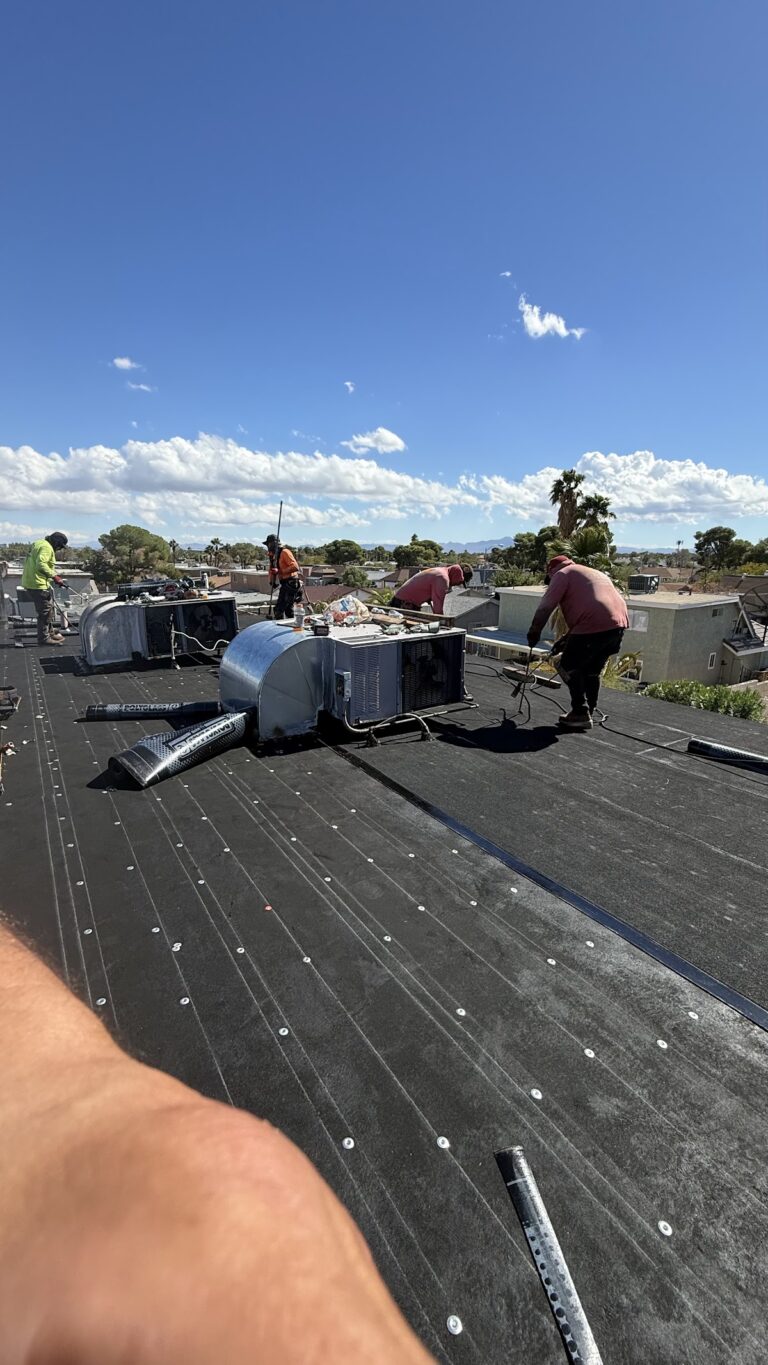 Roofing crew aligning membrane beside HVAC during the Las Vegas home restoration project.