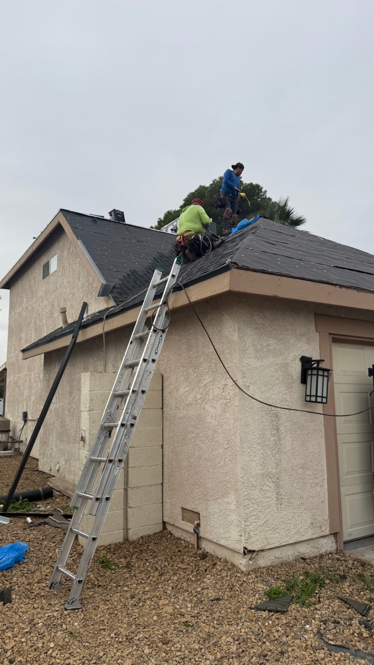 Roofing crew installing shingles beside ladder during the Las Vegas home restoration project.