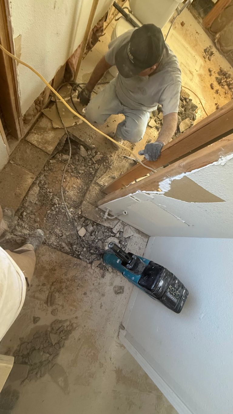 Worker breaking floor around plumbing during the Las Vegas home restoration project.