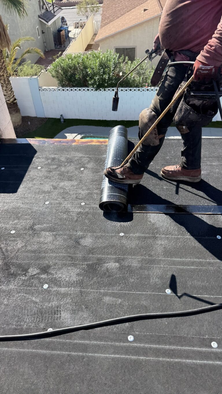 Worker handling roofing roll at roof edge during the Las Vegas home restoration project.