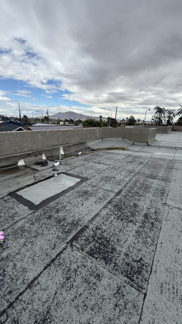 Low-slope roof surface with visible seams, a repair patch and parapet walls