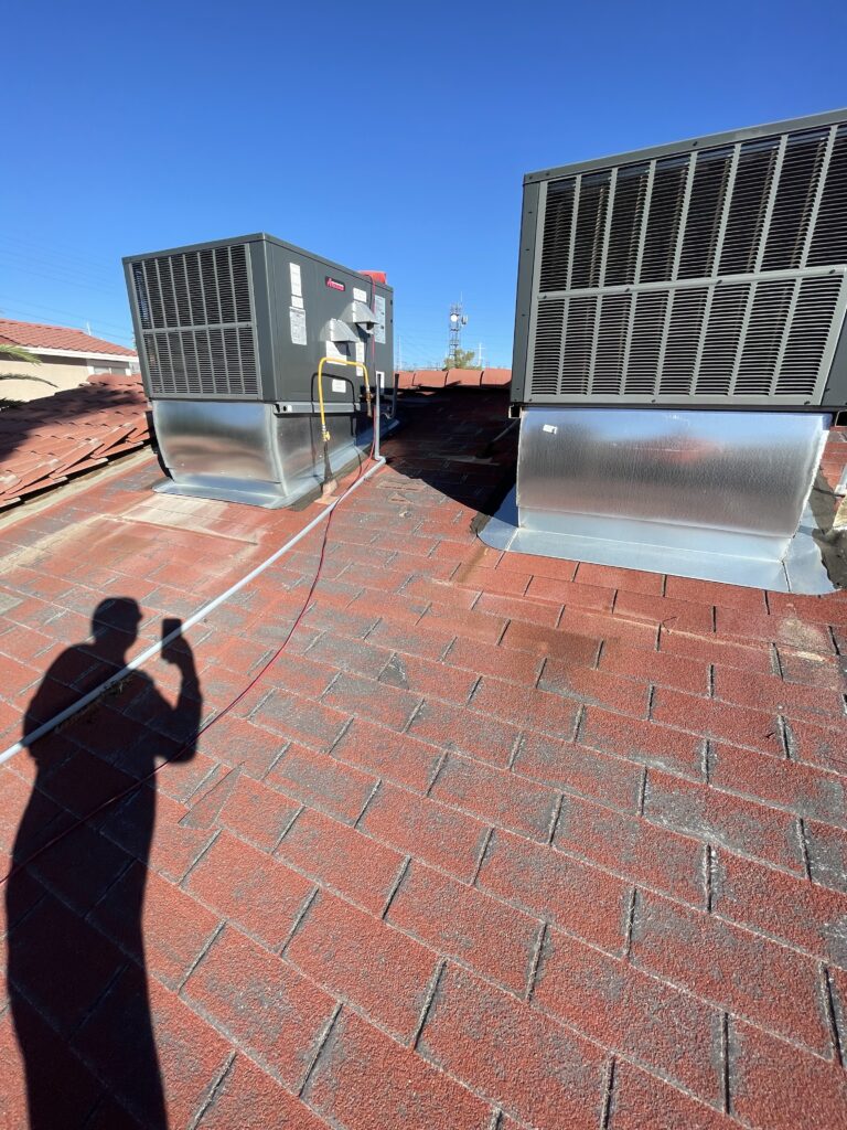 Two rooftop AC units with metal flashing at their bases and surrounding red roofing