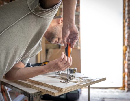 Screwing a self-tapping screw into a metal fastening hole on a wood strip using a screwdriver, the work of a carpenter.
