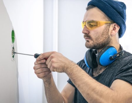 Attractive male electrician repairing an outlet, installing an outlet indoors.